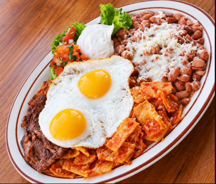 Breakfast plate with two fried eggs over chilaquiles, beans, sour cream and pico de gallo