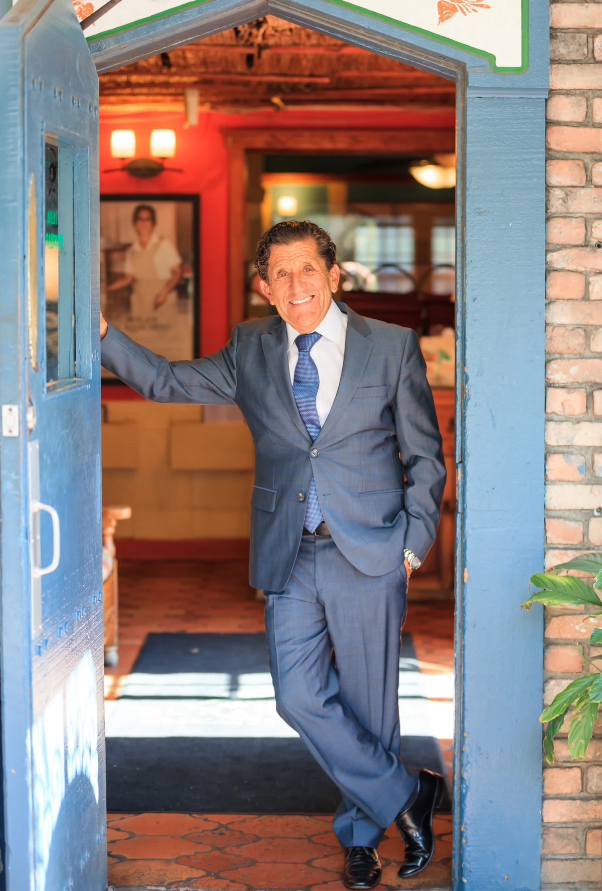 A smiling man in a blue suit welcomes visitors from an open blue doorway