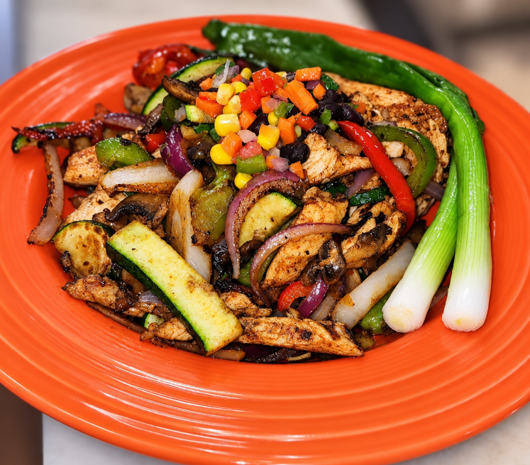 Grilled chicken with zucchini, bell peppers, onions and corn relish served on an orange plate
